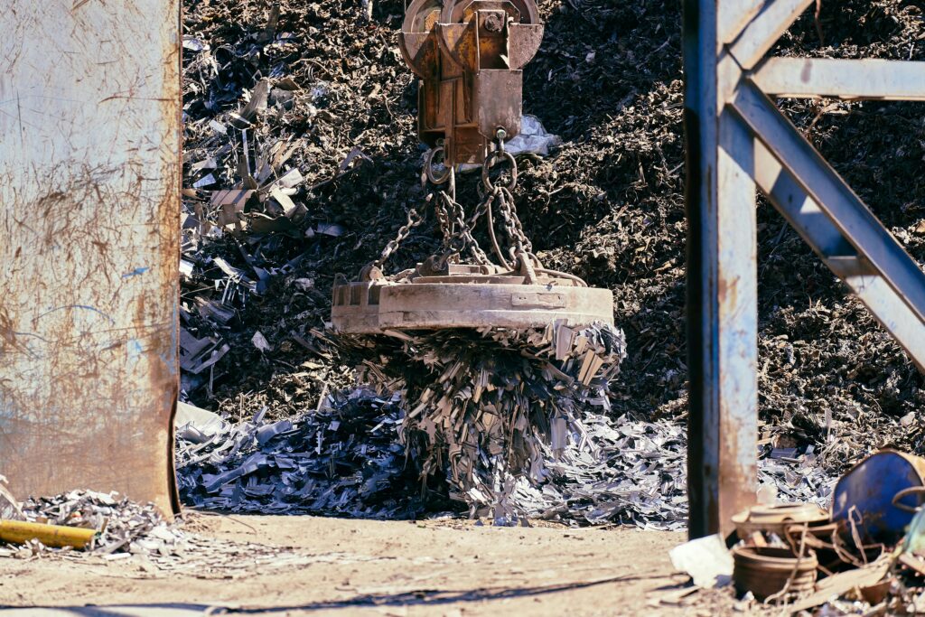Magnet crane lifting scrap metal in a recycling yard.